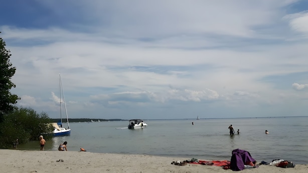 Una playa con barcos, gente y un mar tranquilo.