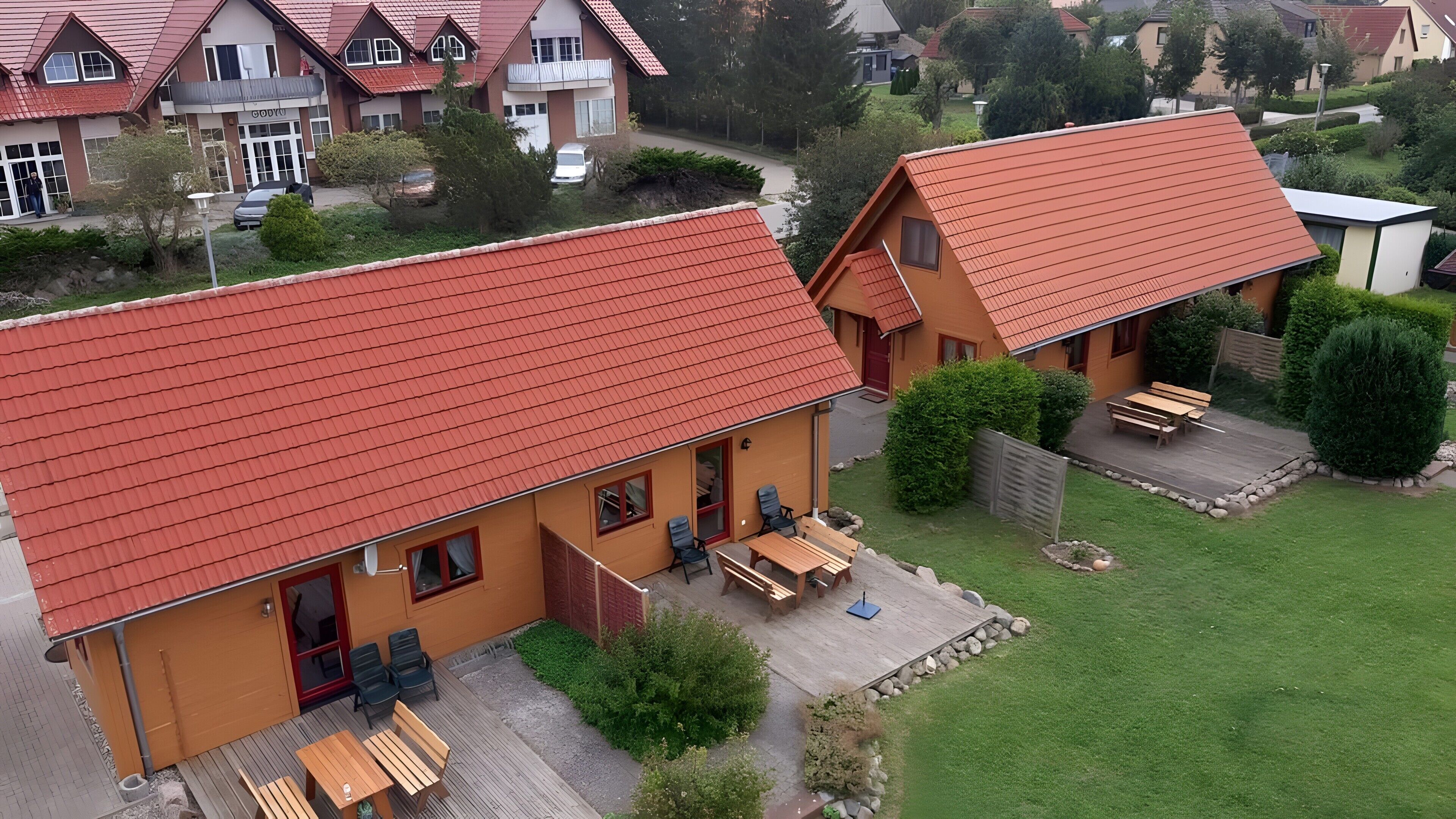 A two-story building with a red roof, a patio with wooden furniture, and a well-maintained lawn.