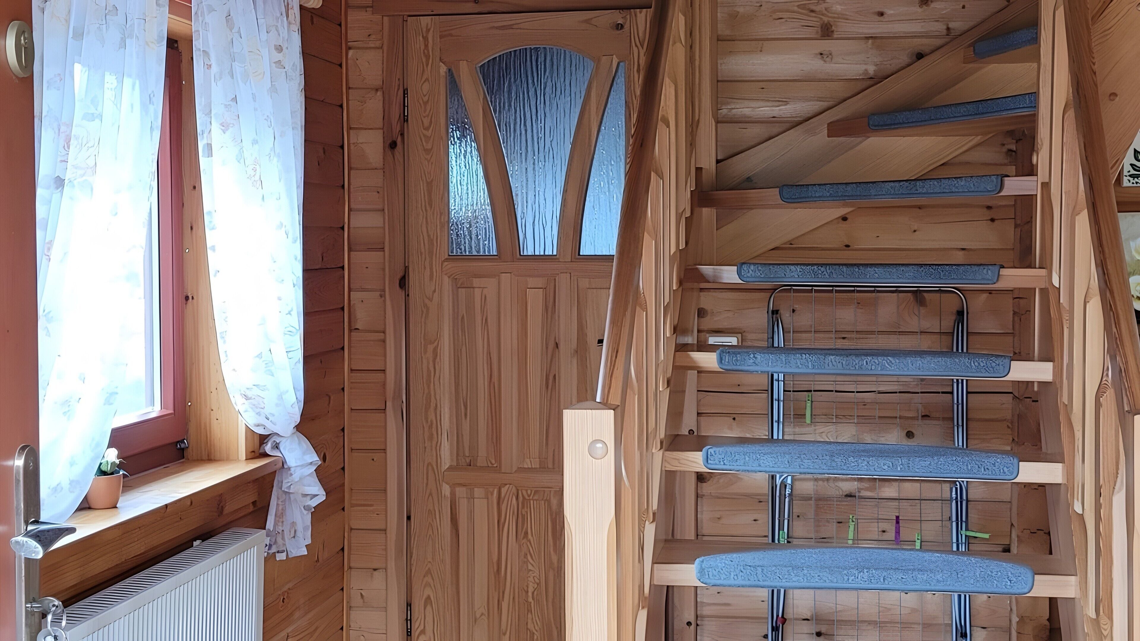 Ein Holzinnenraum mit einer Tür, einem Fenster mit Vorhängen und einer Treppe mit blauen Stufen.