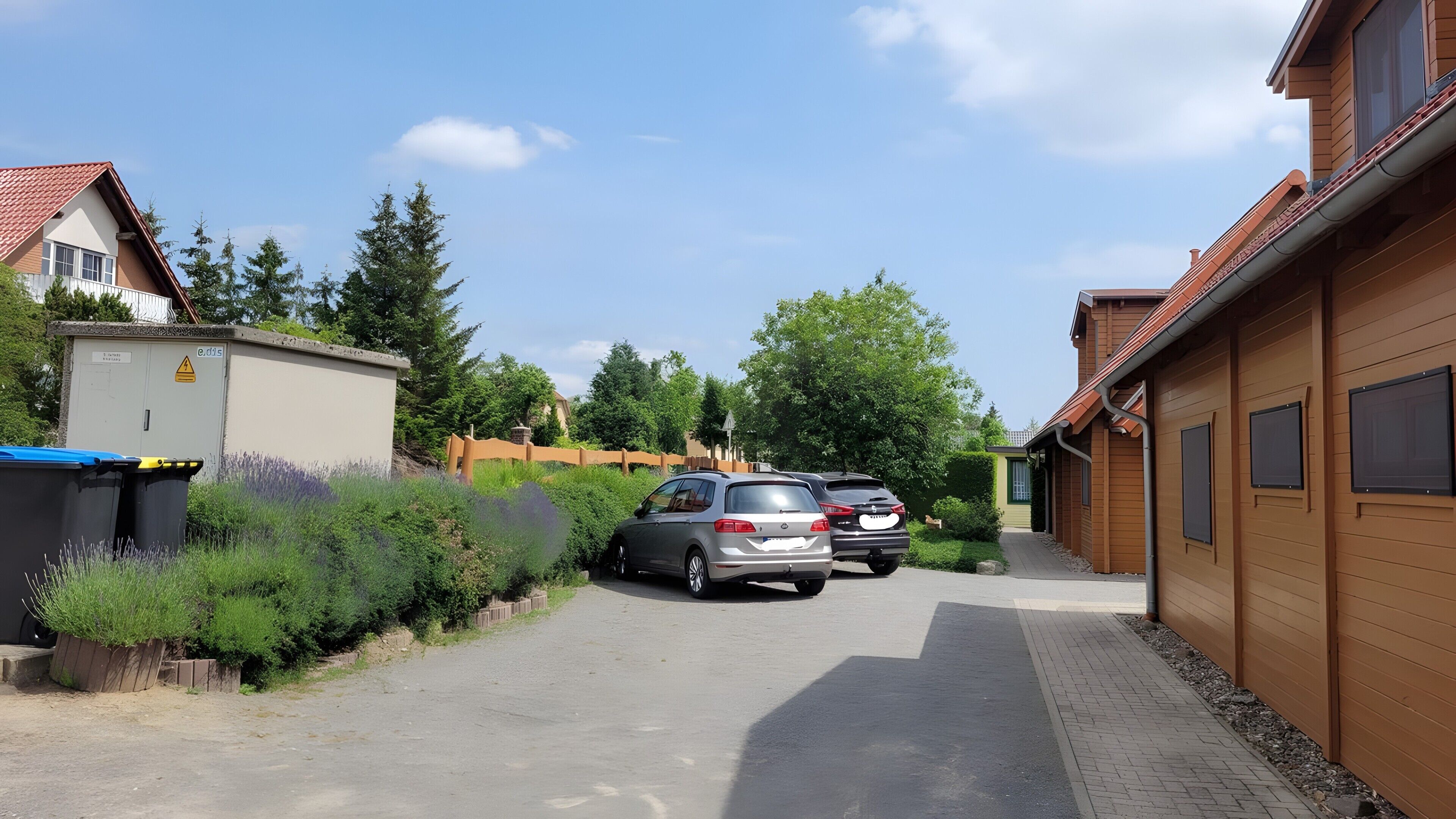 A residential street with parked cars, a utility box, and a wooden house with a tiled roof.