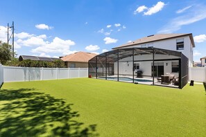 Ein Garten mit Kunstgrasanlage, einer überdachten Terrasse und einem Swimmingpool.