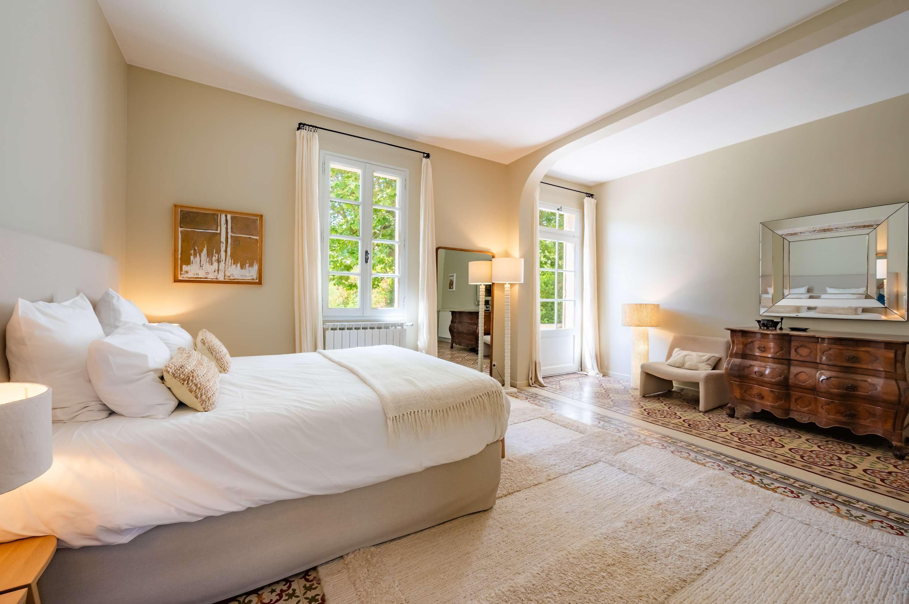 Un dormitorio con una cama grande, un aparador, un espejo y vistas al exterior.