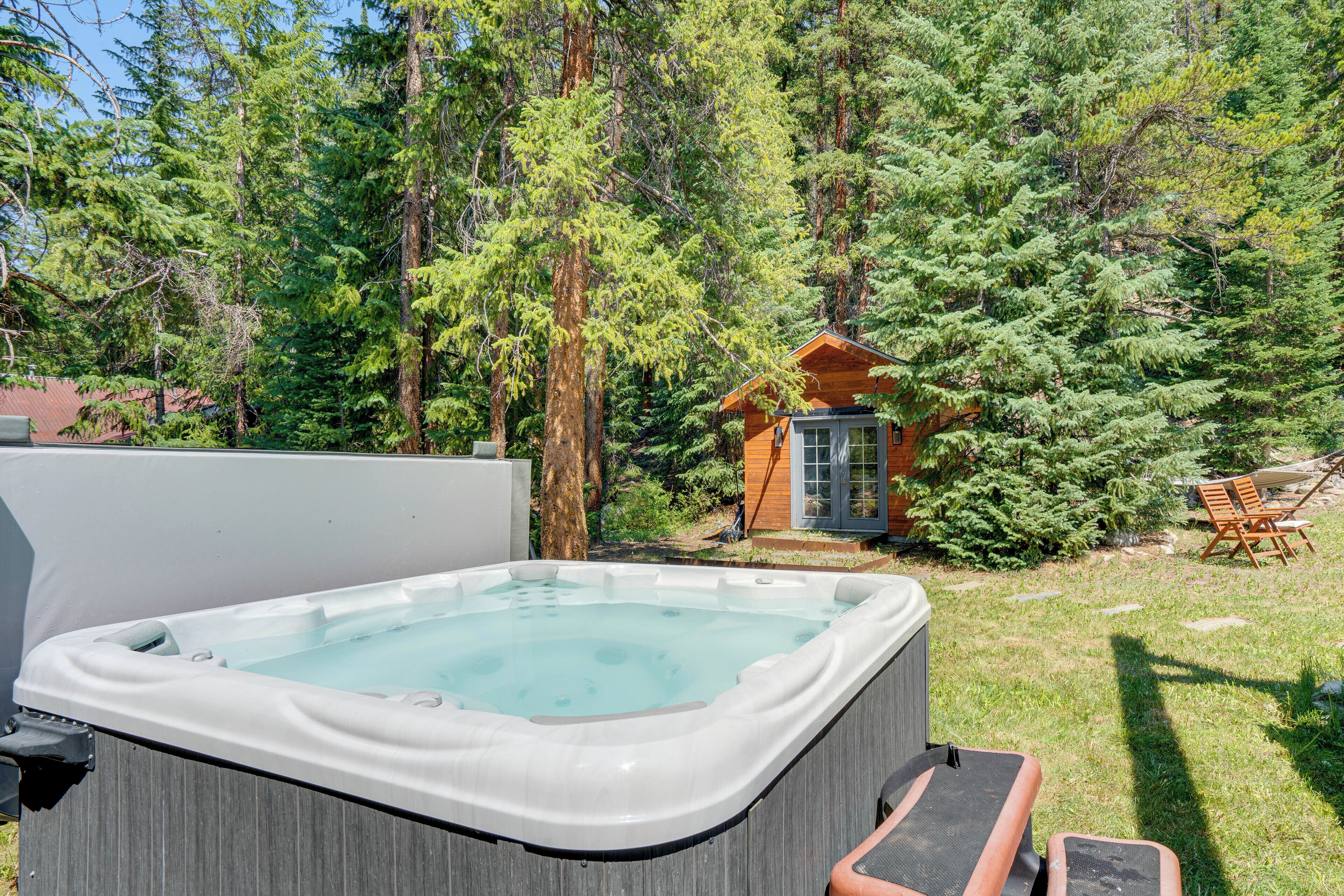 A hot tub in a forested backyard with a wooden cabin in the background.