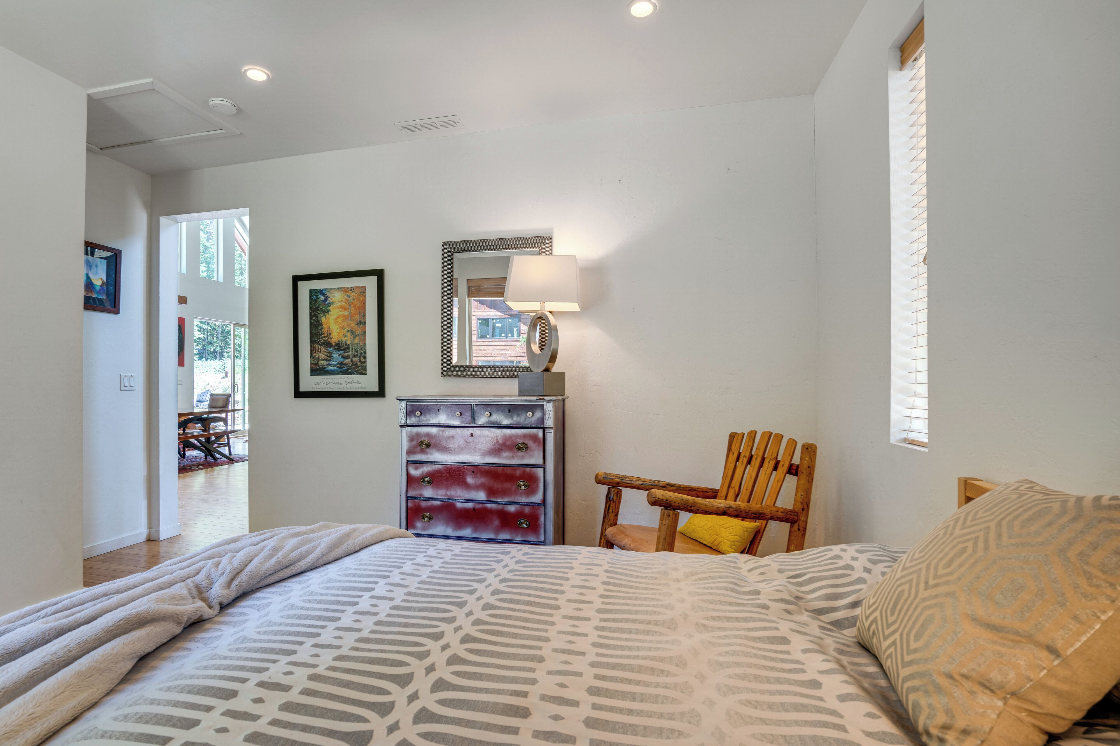 A bedroom with a bed, a wooden chair, a dresser, and artwork on the walls.