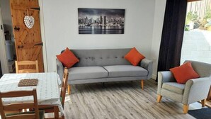 Una sala de estar moderna con un sofá gris, dos sillones, una mesa de comedor con sillas y una pintura de un paisaje urbano.