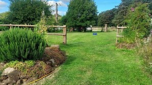 Un área verde y bien cuidada con una cerca de madera, un muro de piedra y diversas plantas.