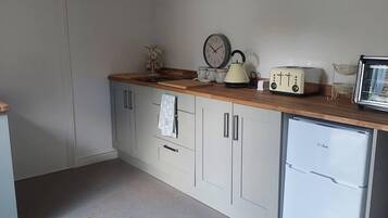 A compact kitchen with white cabinets, a small refrigerator, a wooden countertop, and vintage appliances.