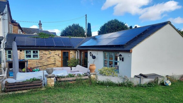 Una casa con techo solar, fachada de ladrillo y jardín delantero.