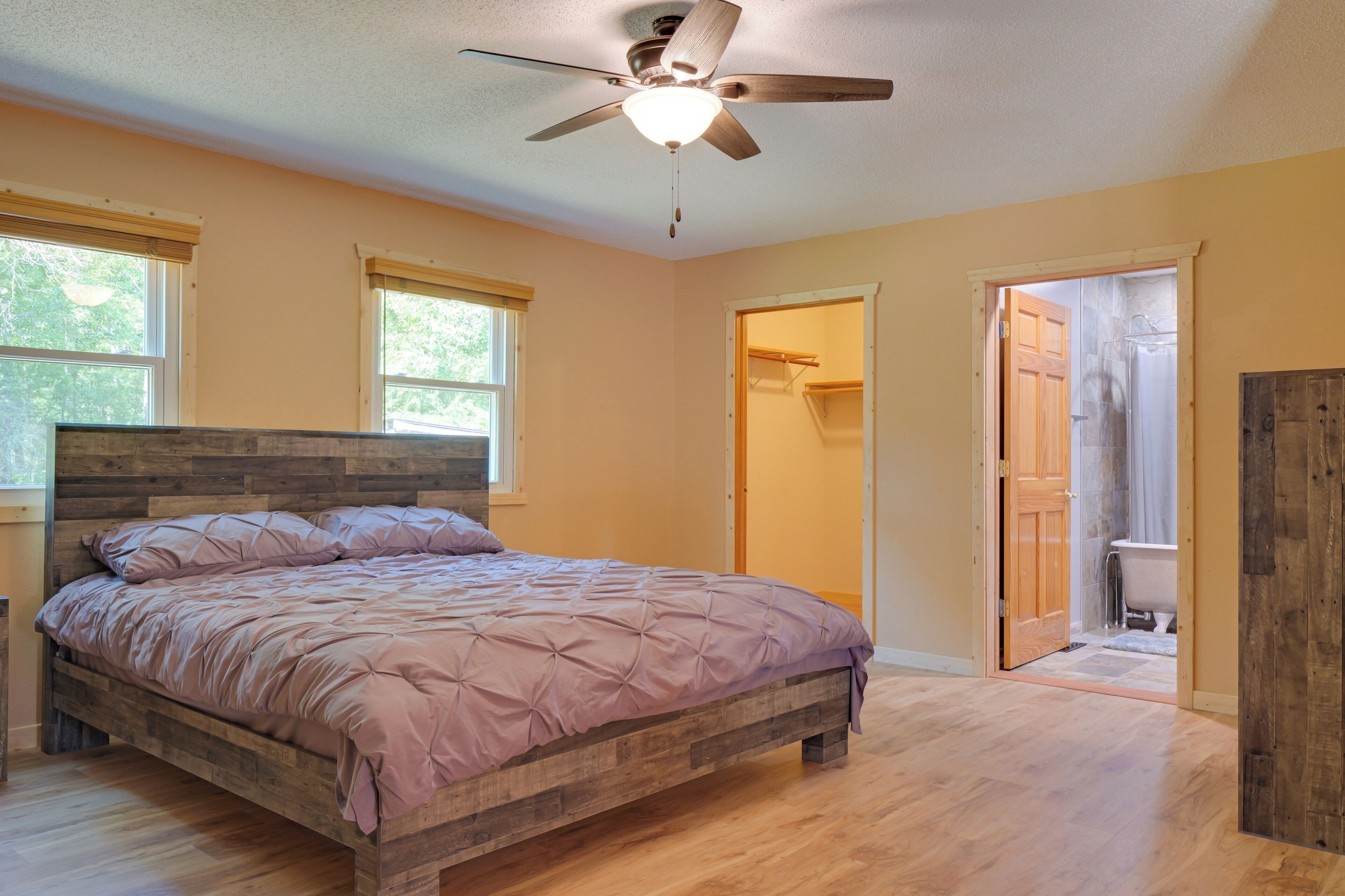 A bedroom with a wooden bed, a ceiling fan, and a view of the bathroom through an open door.