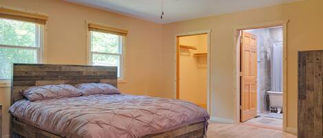 A bedroom with a wooden bed, a ceiling fan, and a view of the bathroom through an open door.