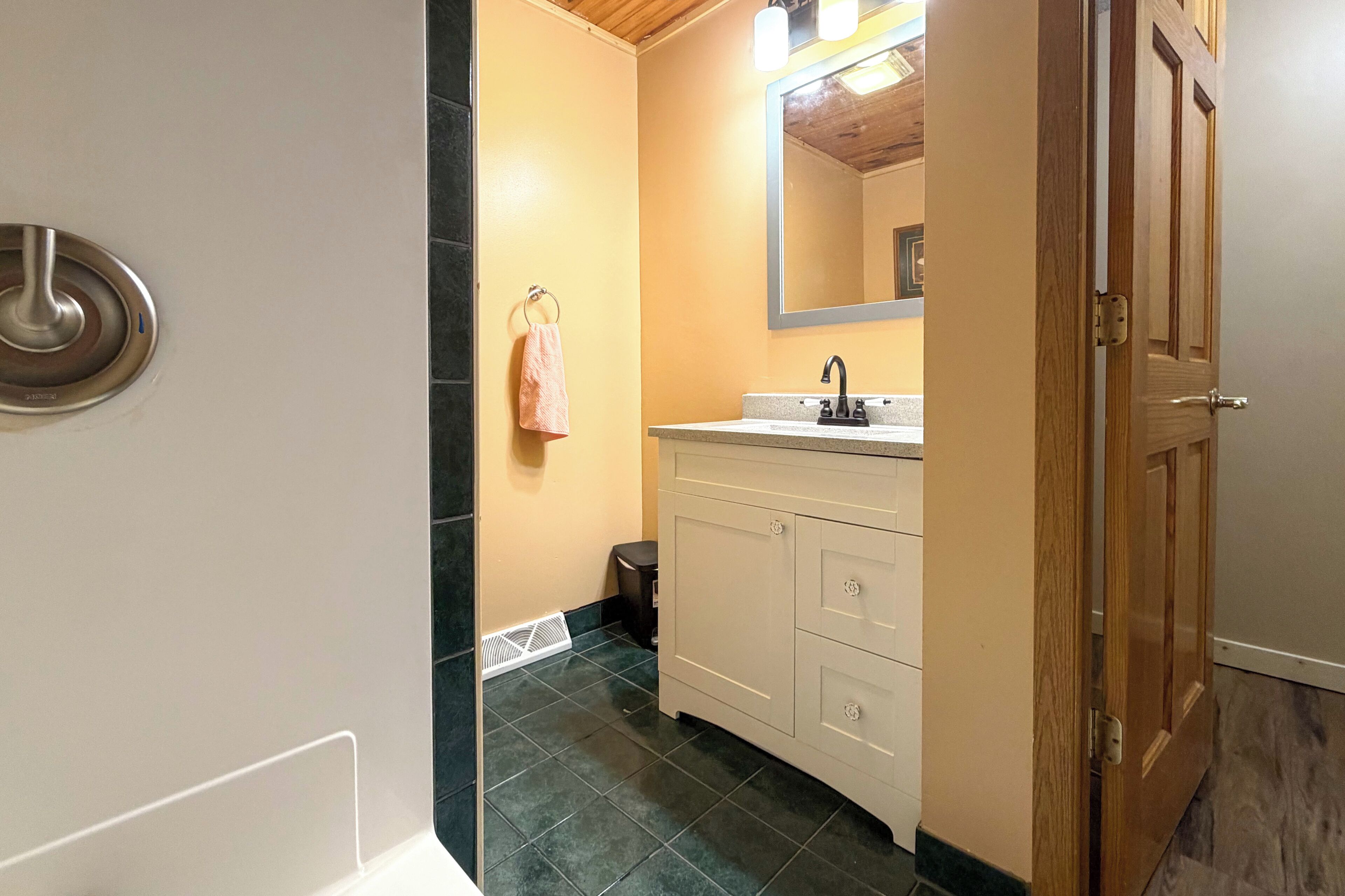 Casa de banho com toucador branco, espelho, toalha pendurada na parede e porta que dá para outro quarto.