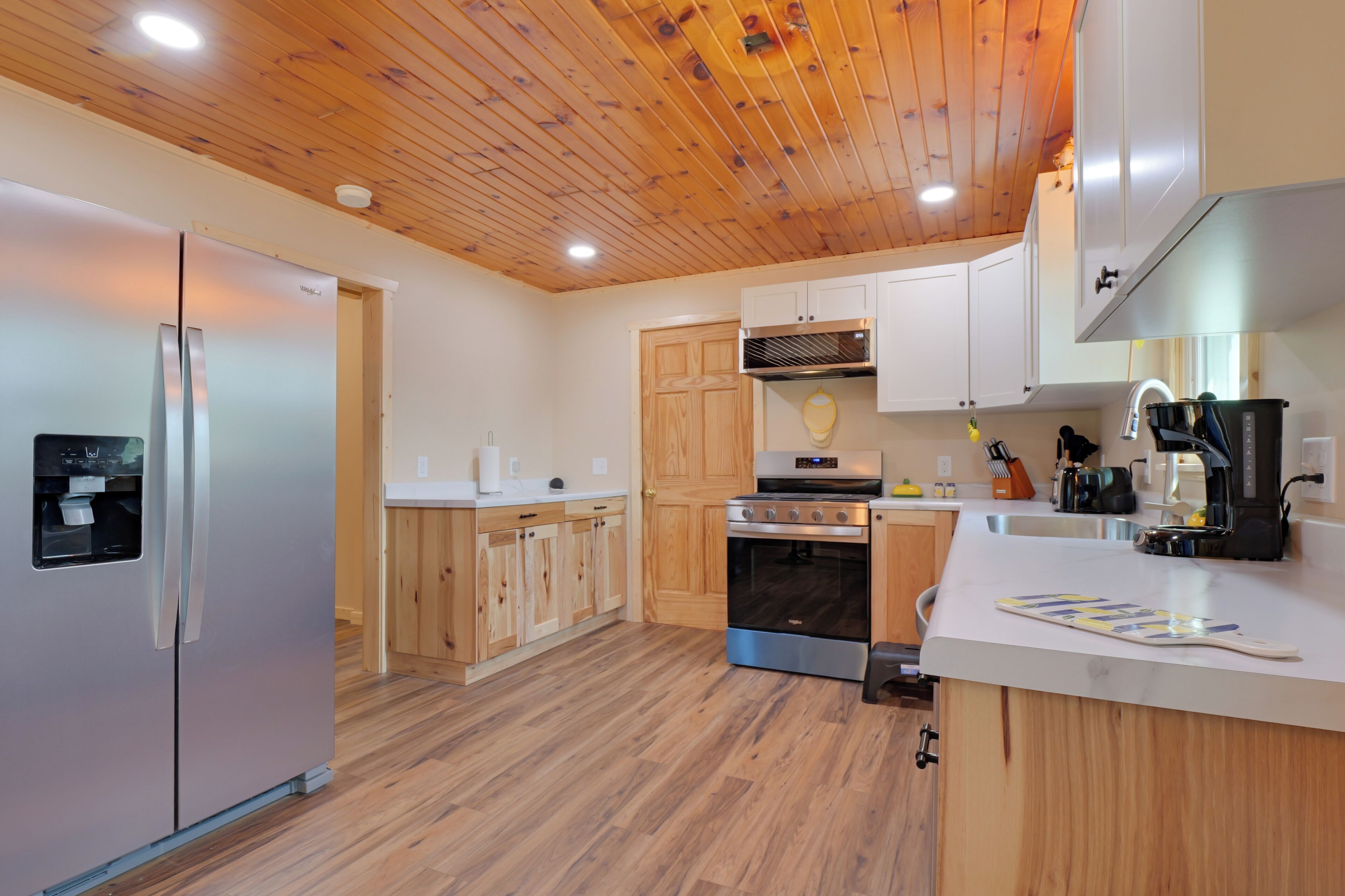 A modern kitchen with wooden cabinets, stainless steel appliances, and a wooden ceiling.