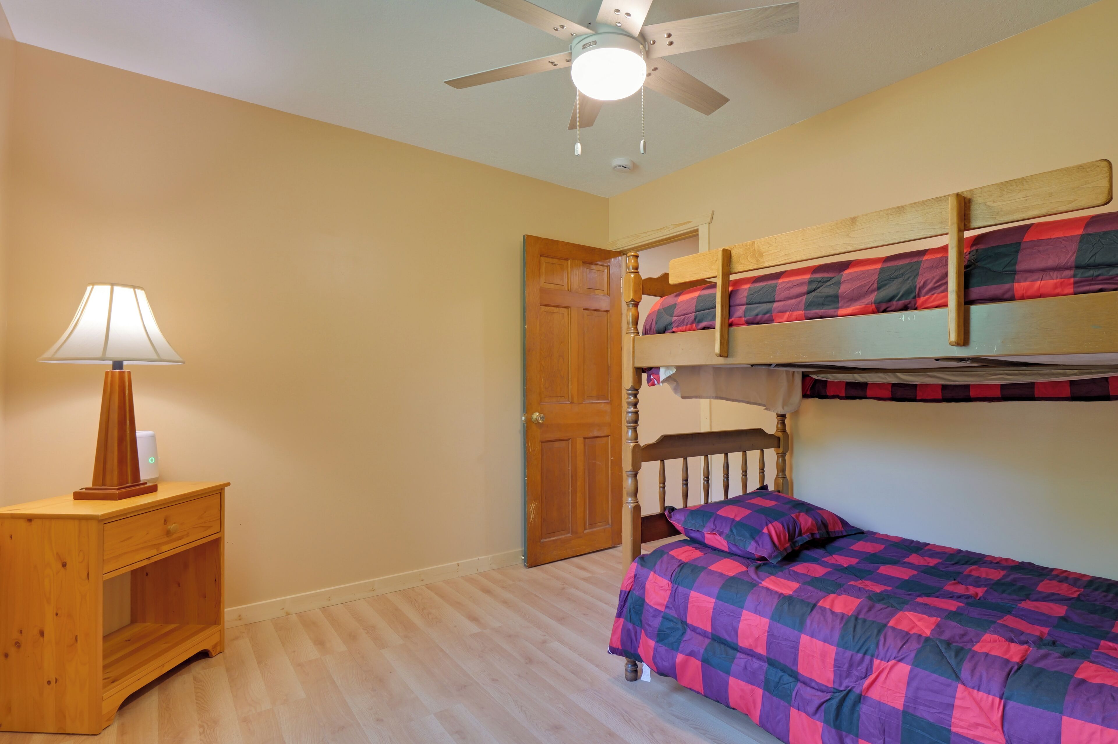 A room with bunk beds, a wooden nightstand with a lamp, and a ceiling fan.