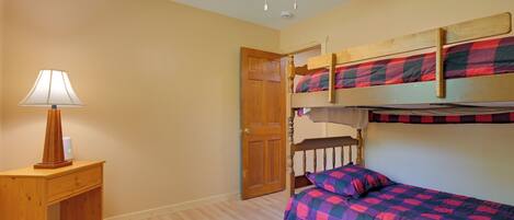 A room with bunk beds, a wooden nightstand with a lamp, and a ceiling fan.