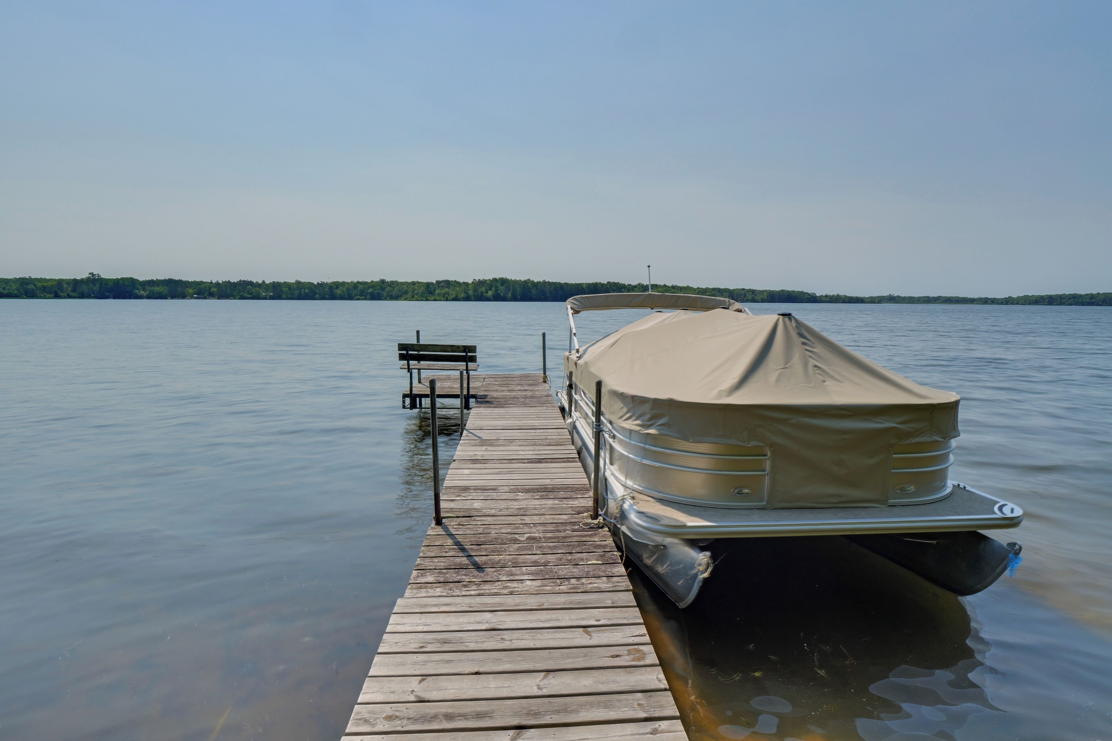 A boat docked on a wooden pier extending into calm water, with a bench and a distant shoreline.