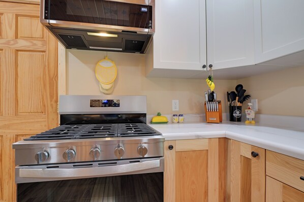 A kitchen with a stainless steel stove, wooden cabinets, a microwave, and a yellow kitchen towel hanging on the wall.