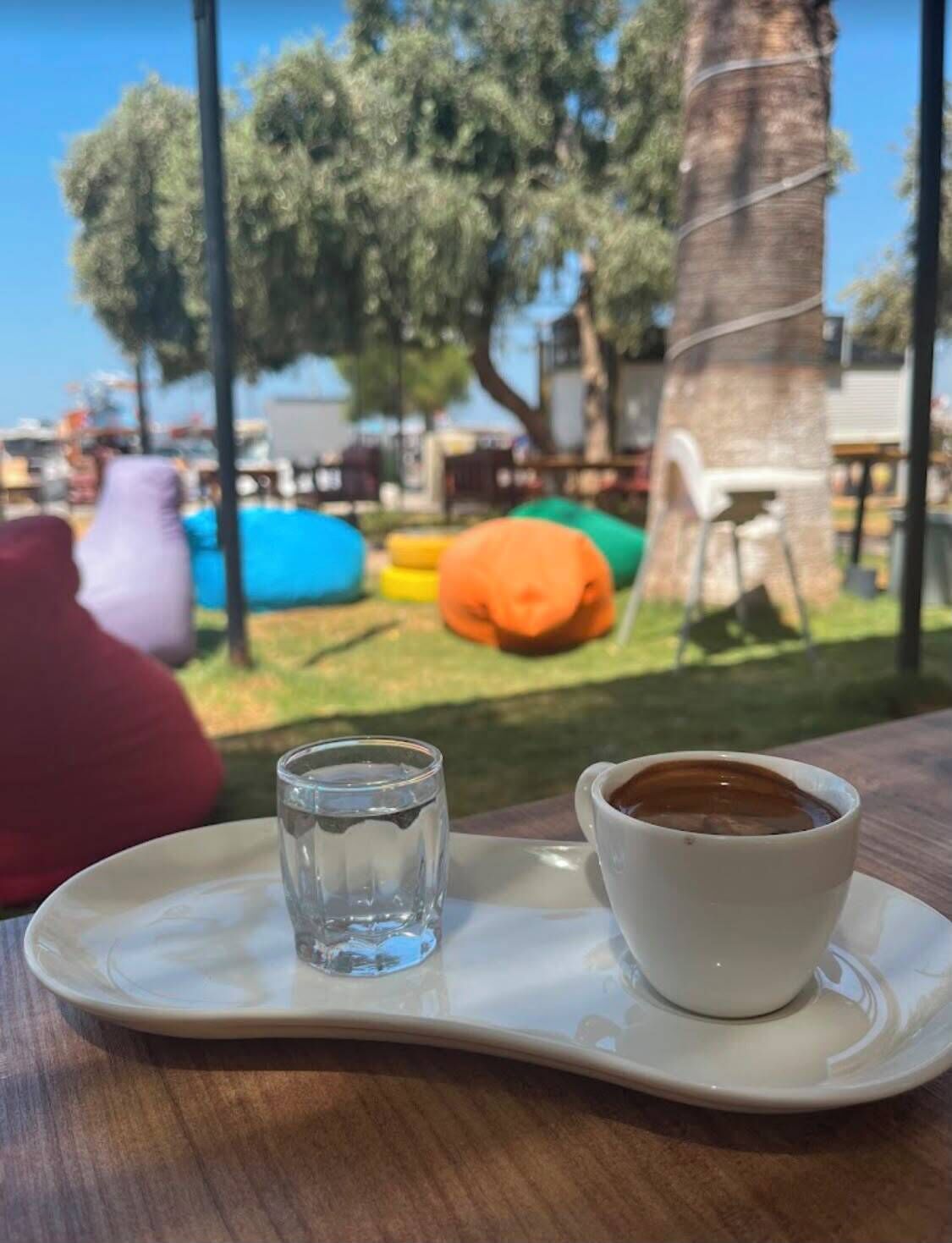 A table with a cup of coffee and a glass of water, a red cushion, and colorful bean bags in the background.
