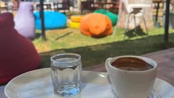 A table with a cup of coffee and a glass of water, a red cushion, and colorful bean bags in the background.