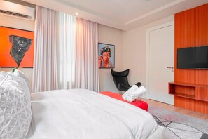 Een moderne hotelkamer met een groot bed, een flatscreen televisie, een rode fauteuil en kunstwerken aan de muur.