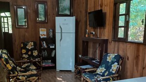 A wooden-paneled room with a refrigerator, two chairs with floral upholstery, a table, and a television on the wall.