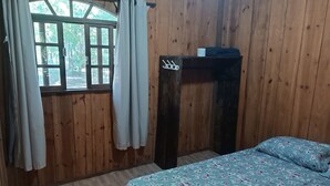 A wooden room with a bed, a window with curtains, and a wooden cabinet with hooks.