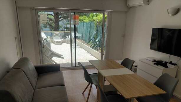 A modern room with a sofa, a dining table with chairs, a TV, and a sliding glass door leading to an outdoor area with chairs. - 2-room apartment with a terrace (Cannes)