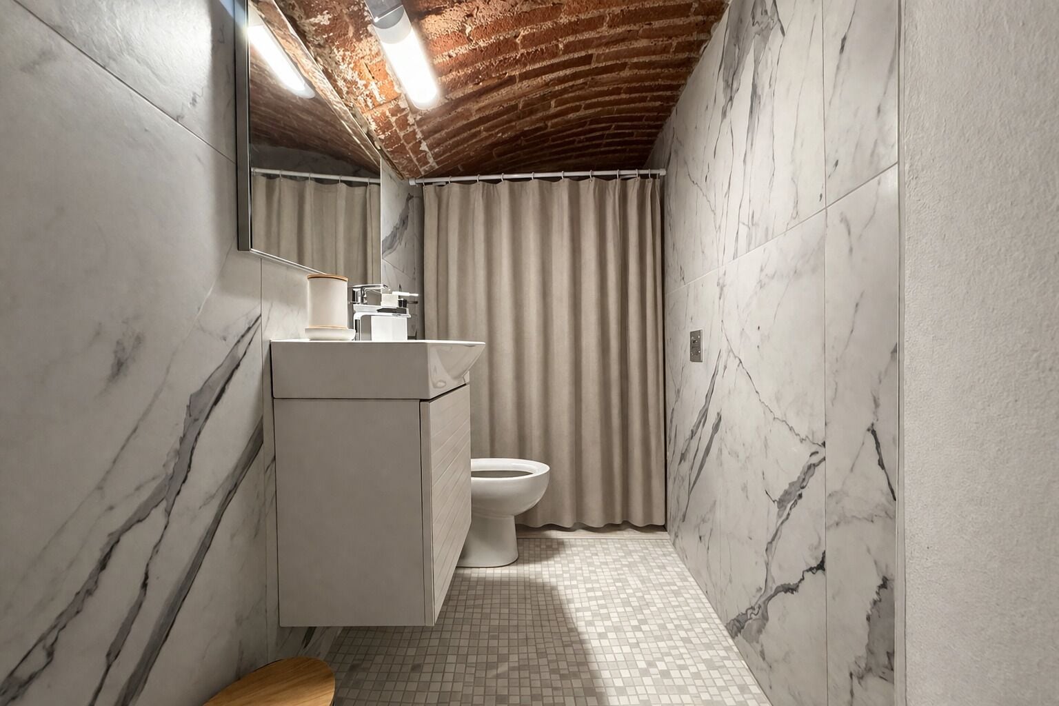A bathroom with a marble wall, a wooden bench, a toilet, and a sink with a mirror.
