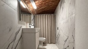 A bathroom with a marble wall, a wooden bench, a toilet, and a sink with a mirror. - Elegant 5-day loft, Milan Dateo, tricolor (Milano)