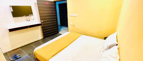 A hotel room with a bed, a TV, a desk, and a door.