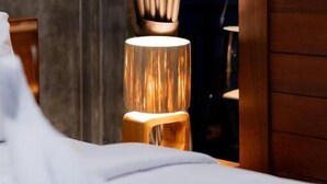 A bed with white linens, a wooden nightstand, and a lamp with a cylindrical shade. - Joni Ubud Hostel (Mas)