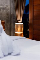 Una cama con sábanas blancas, una mesita de noche de madera y una lámpara con pantalla cilíndrica.