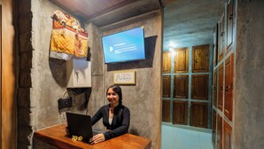 A reception desk with a laptop, a mounted television displaying a message, and a framed welcome sign. - Joni Ubud Hostel (Mas)