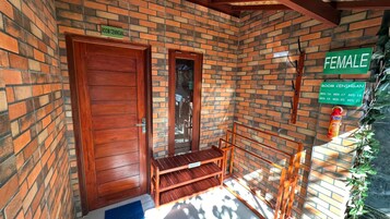 Habitación de paredes de ladrillo con puerta de madera, un banco y un letrero que indica 'ROOM CENINGAN' y 'FEMALE'.