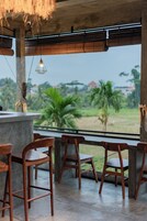 Un área de estar al aire libre con sillas de madera y una mesa de hormigón, con vistas a un paisaje verde con árboles y edificios.