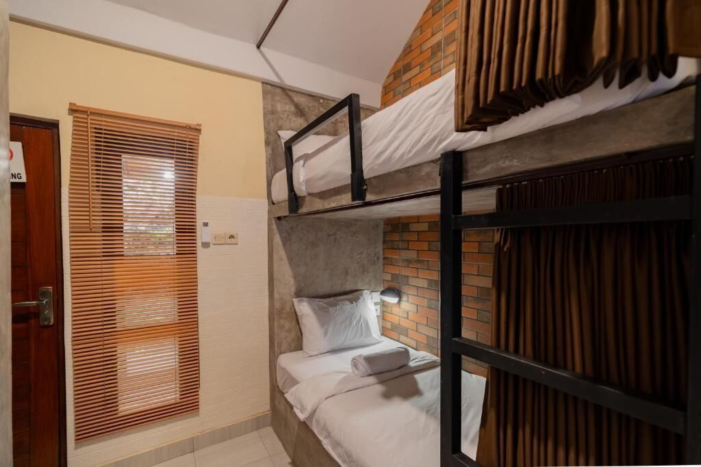 Une chambre avec un lit superposé, un mur en briques, une porte avec une pancarte et une fenêtre avec des stores.