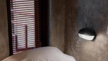 A bed with white linens, a rolled towel, and a wall-mounted light fixture.