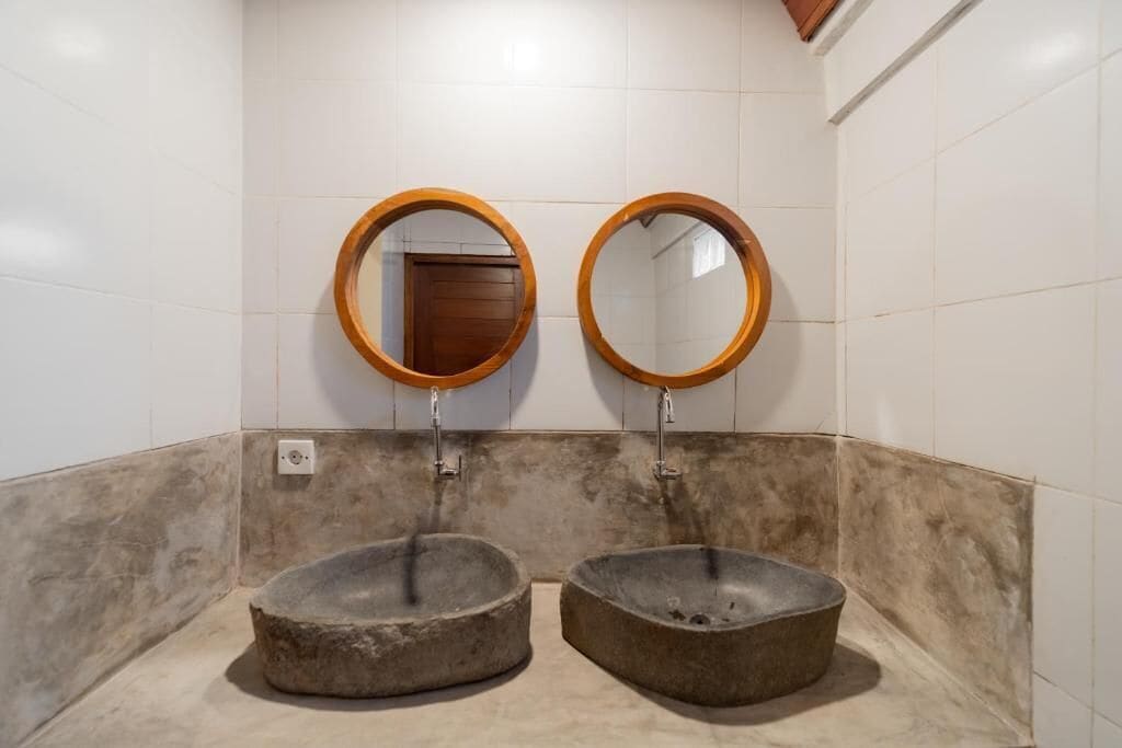 Un baño con dos lavamanos de piedra y dos espejos con marco de madera en la pared.