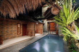 Una piscina interior con pared de ladrillo, techo de paja y plantas tropicales.