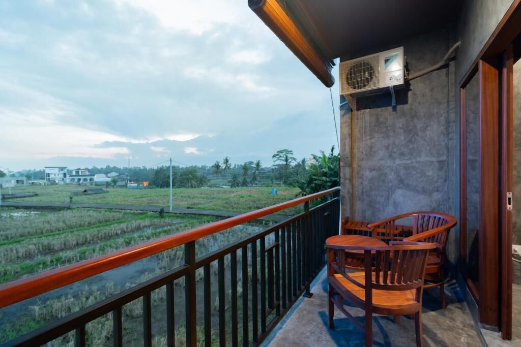 A balcony with a view of a rice field, a table and chairs, and an air conditioning unit.