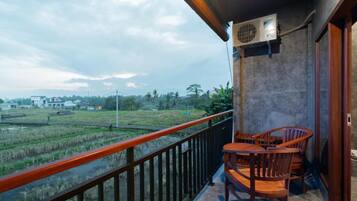 A balcony with a view of a rice field, a table and chairs, and an air conditioning unit.