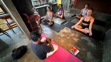 A yoga class in a room with a concrete floor, yoga mats, and participants seated on mats.