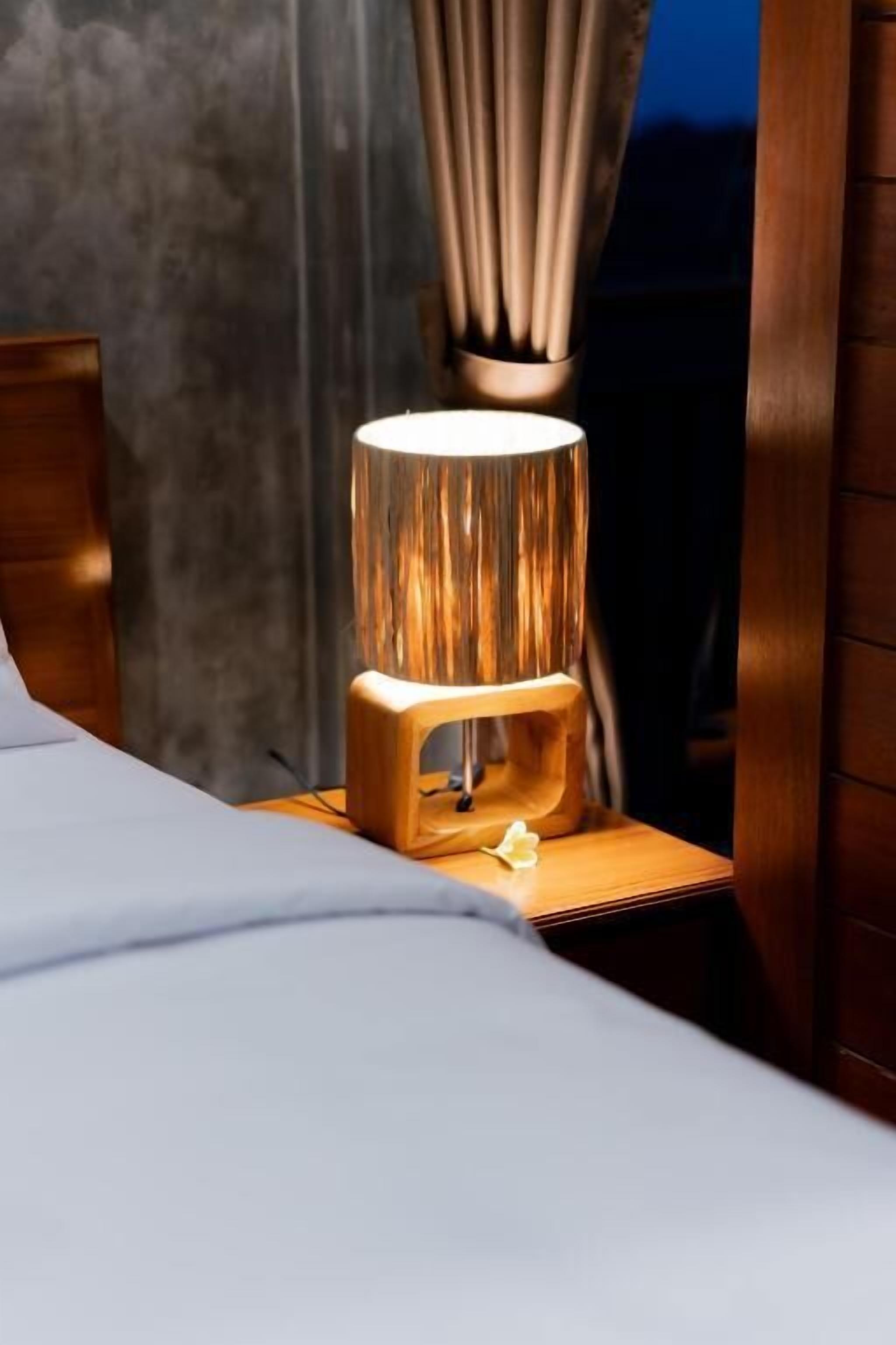 Ein Bett mit einem Nachttisch aus Holz, einer Lampe und einem Vorhang.