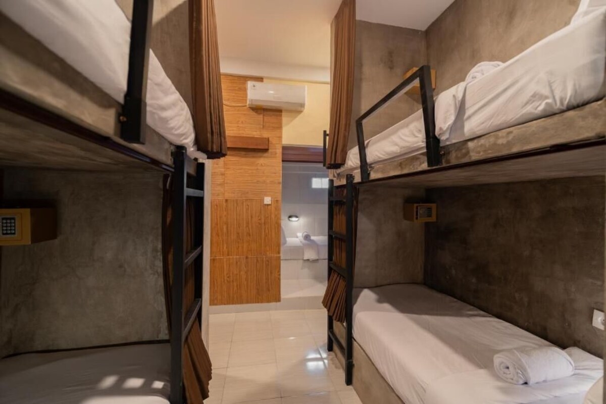 A bunk bed room with a wooden wall, a small bathroom, and a ceiling fan.