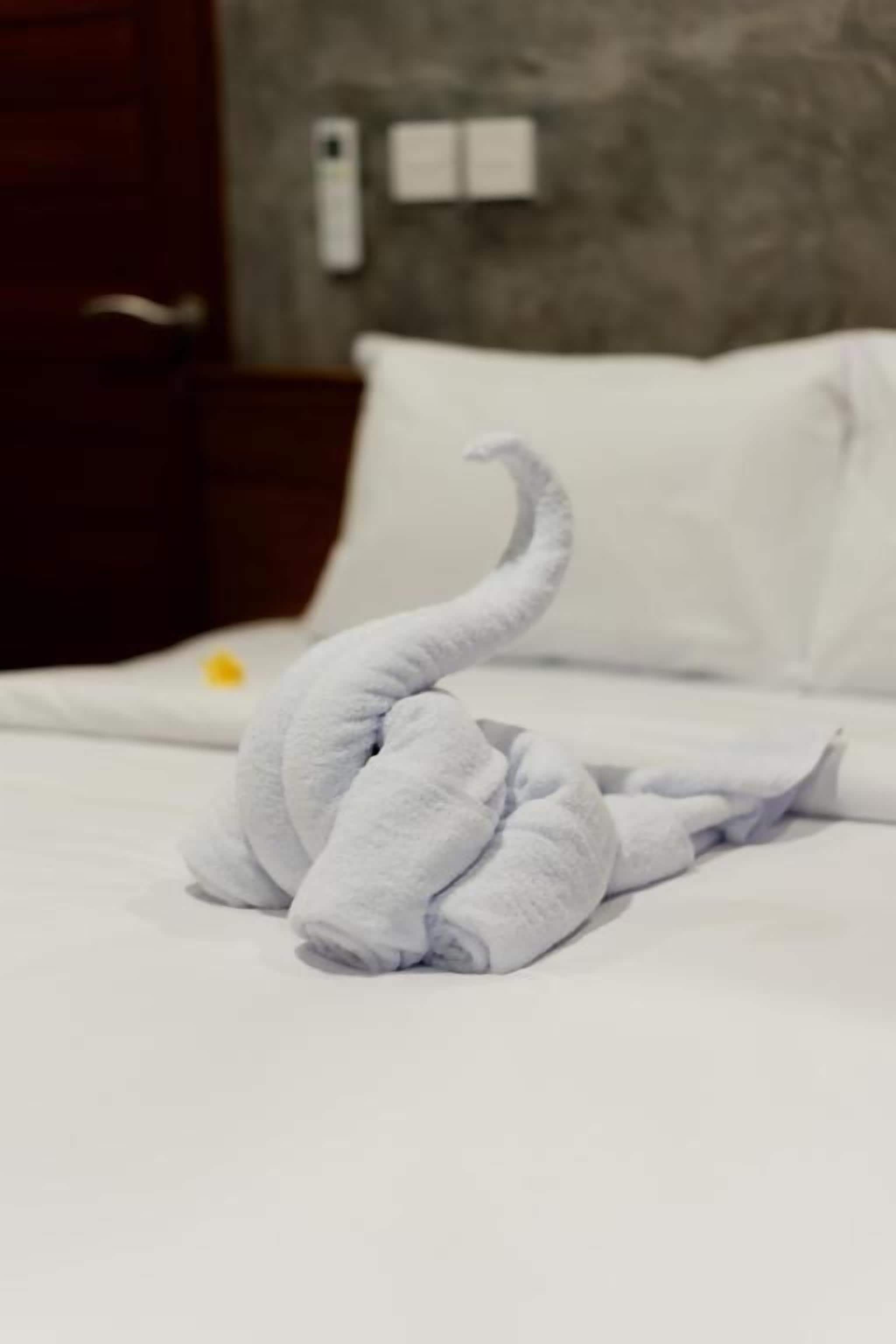 A neatly made bed with a towel arranged in a swan shape.