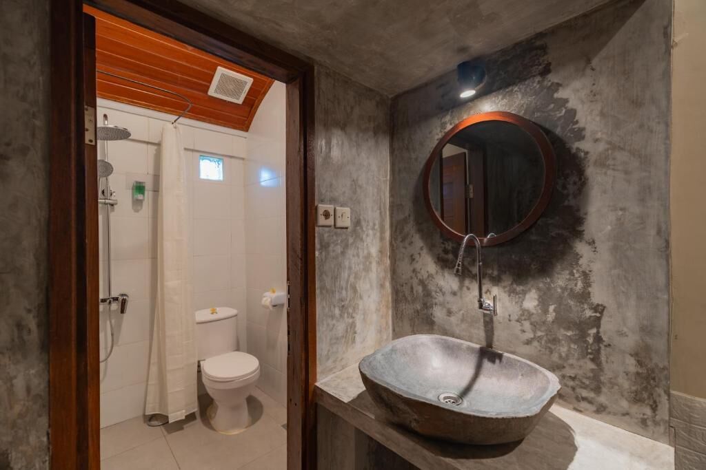 A bathroom with a rustic design, featuring a large, round sink with a mirror above it and a toilet visible in the background.