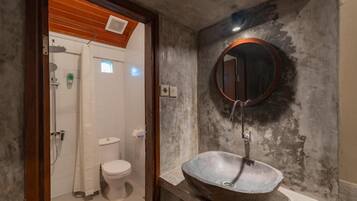 A bathroom with a rustic design, featuring a large, round sink with a mirror above it and a toilet visible in the background.