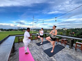 Un grupo de personas practicando yoga en colchonetas al aire libre, con vista a un paisaje verde y edificios al fondo.