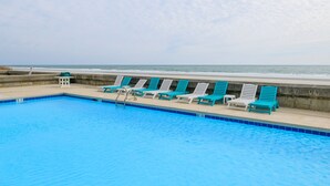 En swimmingpool med blå kakelplattor, omgiven av solstolar och en betongmur.