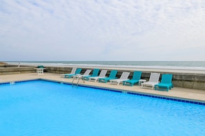 A swimming pool with blue tiles, surrounded by lounge chairs and a concrete wall. - 1st Floor, 2BR Oceanfront Condo, Shared Pool - Sand Dollar 103 (Murrells Inlet)