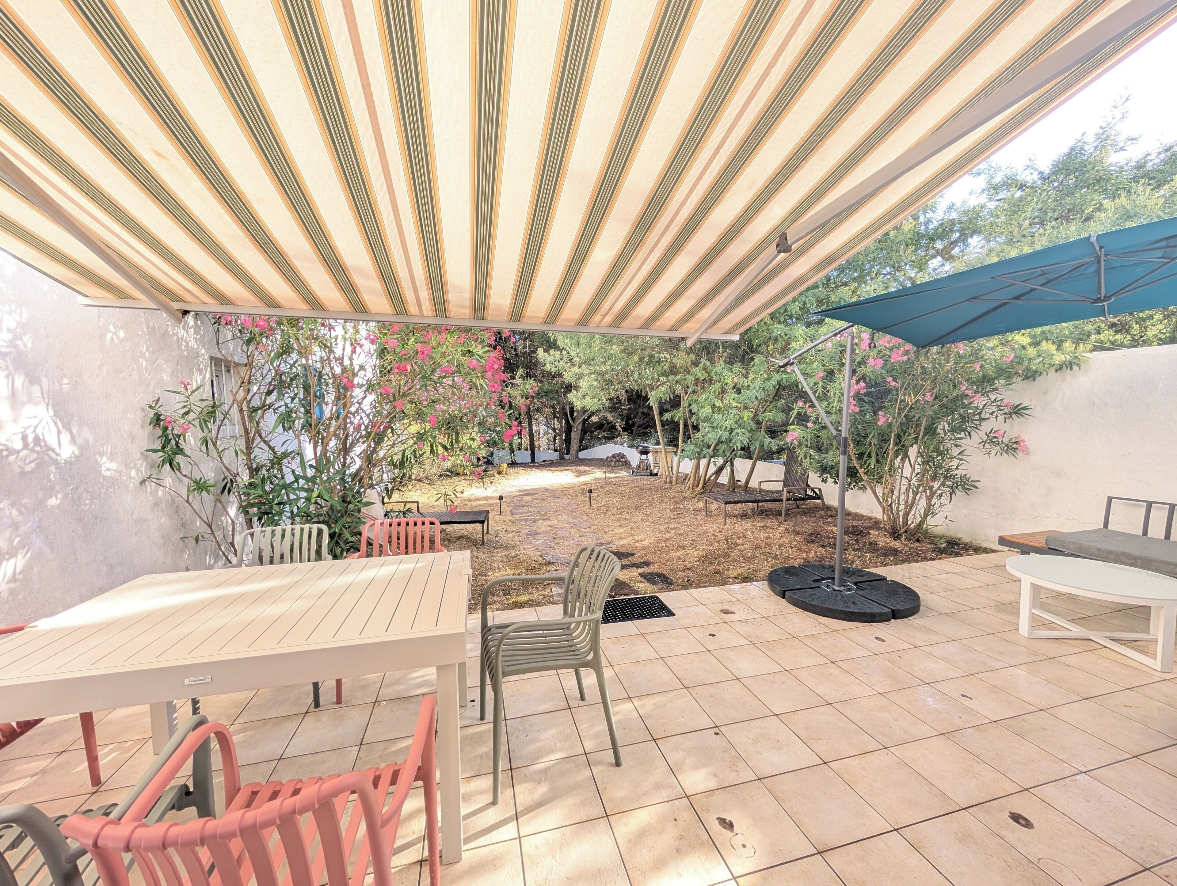 An outdoor patio with a table and chairs, a covered seating area, and a garden with trees and shrubs.